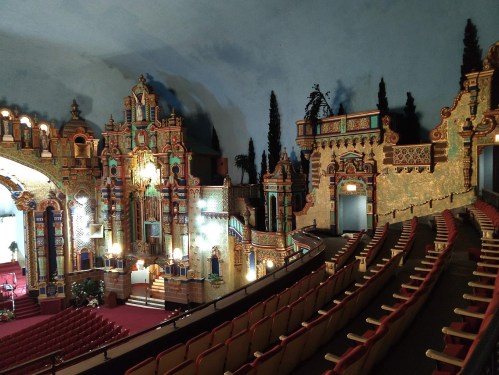 Interior of a beautifully ornate theater with colorful decorations and empty red seats, showcasing a grand stage.
