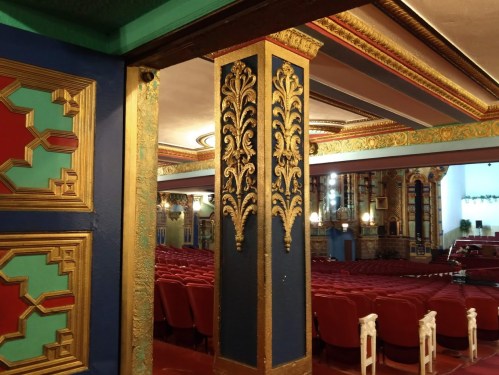 Interior of a vintage theater featuring ornate columns and a view of red seating in the background.