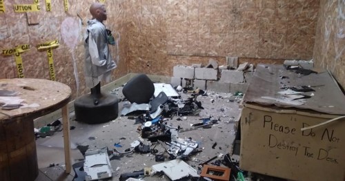 A messy room with scattered debris, a mannequin on a pedestal, and a sign reading "Please Do Not Destroy The Desk."