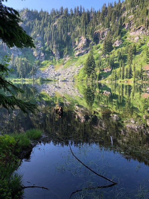 A serene lake surrounded by lush greenery and rocky cliffs, reflecting the landscape in calm waters.