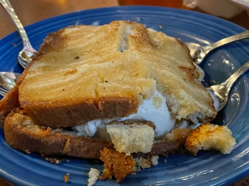 A slice of dessert with layers of cake and ice cream, served on a blue plate with two spoons beside it.