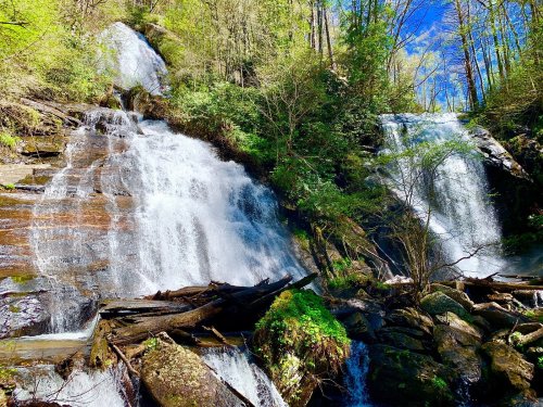 A scenic view of two waterfalls cascading over rocky cliffs, surrounded by lush greenery and blue skies.