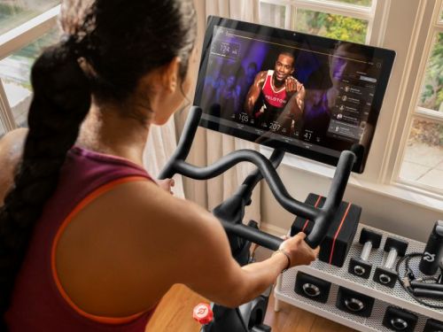 A person rides a stationary bike while following a virtual workout on a screen, with fitness equipment nearby.