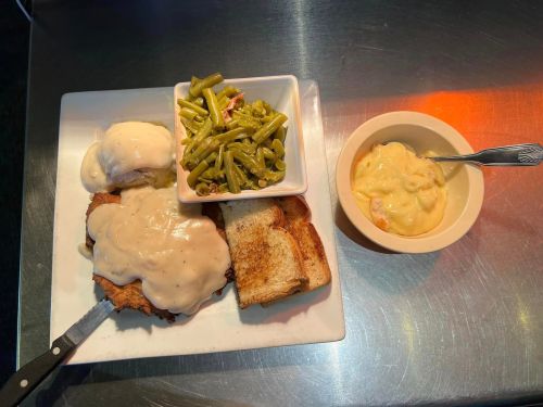 A plate with fried chicken smothered in gravy, green beans, toast, and a bowl of creamy macaroni and cheese.