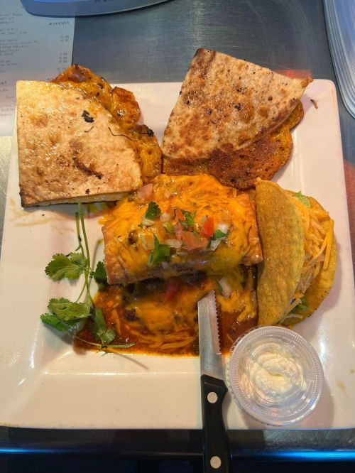 A plate featuring a cheesy enchilada, taco, and quesadilla, garnished with cilantro and served with sour cream.