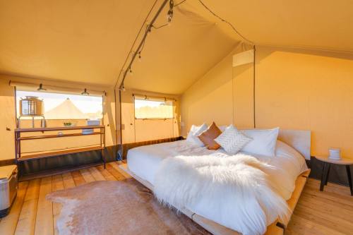 Cozy glamping tent interior with a large bed, soft blankets, and warm lighting, surrounded by large windows.