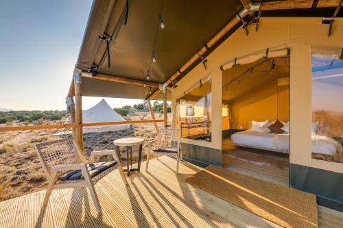 A cozy glamping tent with a wooden deck, featuring a bed, chairs, and scenic views of the surrounding landscape.