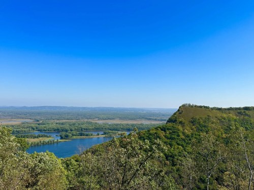 A scenic view of a river winding through lush green hills under a clear blue sky.