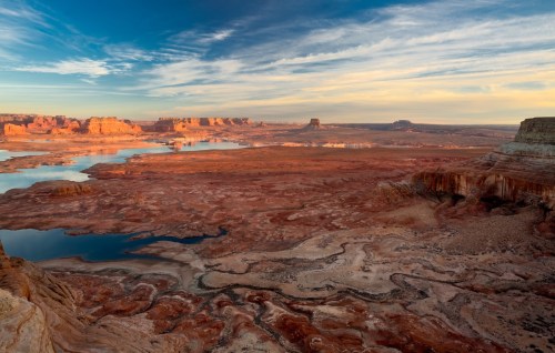 A vast desert landscape with winding rivers, rocky formations, and a colorful sky at sunset.