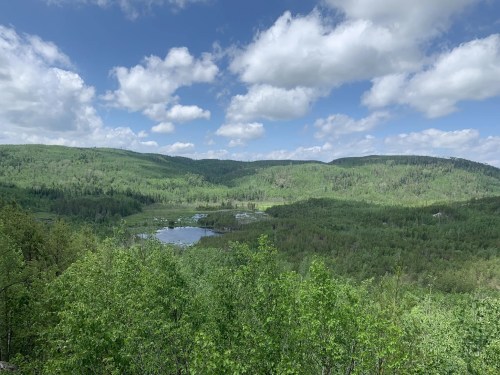 Lush green landscape with rolling hills, a serene lake, and a cloudy blue sky.