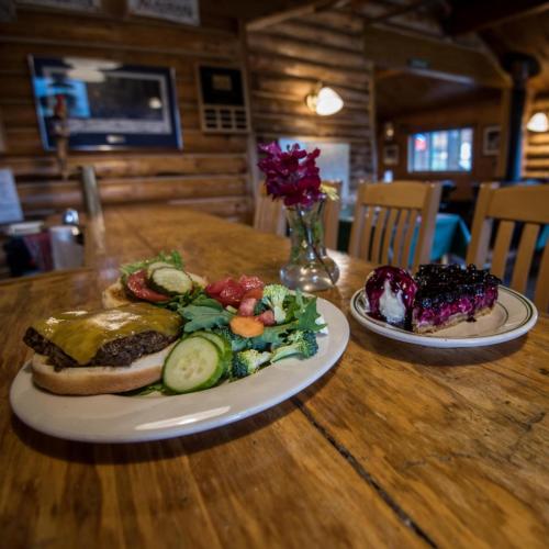 A plate with a burger, fresh vegetables, and a dessert on a wooden table in a cozy restaurant setting.