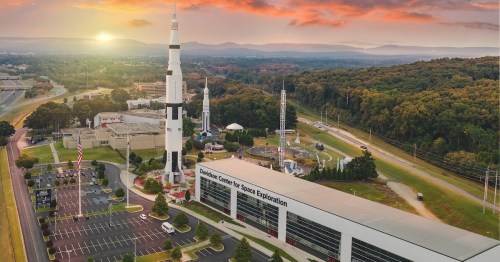 Aerial view of the U.S. Space & Rocket Center with a rocket display and mountains in the background at sunset.