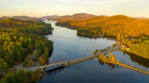 Aerial view of a serene lake surrounded by autumn-colored hills and a small bridge connecting the shore.