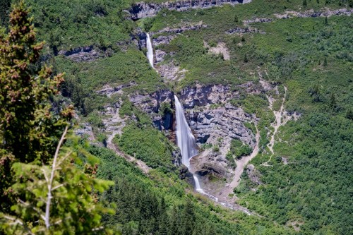 A scenic view of a waterfall cascading down a rocky cliff, surrounded by lush green vegetation and trees.