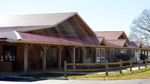 A building with a red metal roof and wooden accents, surrounded by a grassy area and a wooden fence.