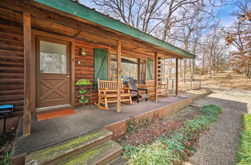 A rustic cabin porch with rocking chairs, surrounded by trees and a gravel path.