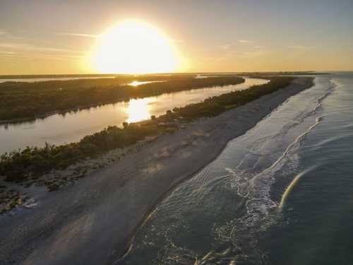 Aerial view of a serene beach at sunset, with gentle waves and a river reflecting the golden sun.