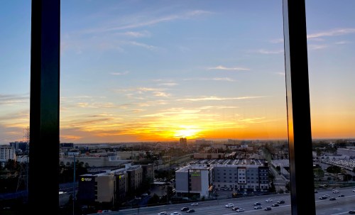 Sunset view from a high-rise window, showcasing a city skyline and colorful sky with clouds.