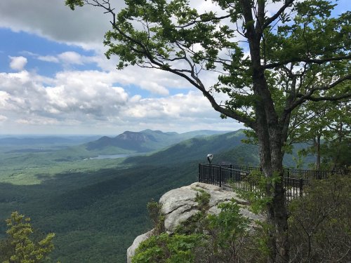 A scenic view from a rocky overlook, featuring lush green mountains and a cloudy sky in the background.