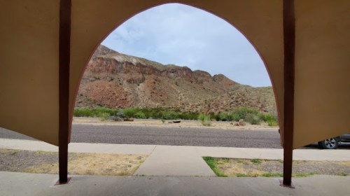 View of a rocky landscape framed by an archway, with a road and greenery in the foreground.