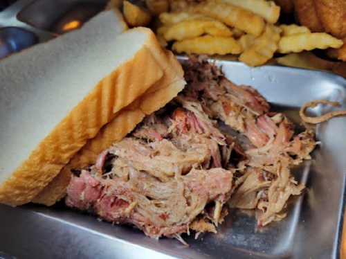 A plate with pulled pork, two slices of white bread, and a side of crinkle-cut fries.