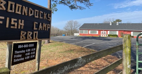Sign for Boondocks Fish Camp BBQ with a view of the building and empty parking lot on a clear day.