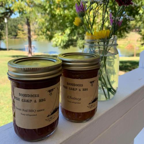 Two jars of homemade sauces, one labeled BBQ sauce and the other chutney, with a flower vase in the background.