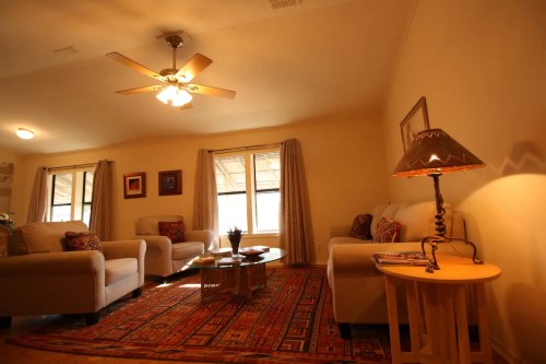 Cozy living room with two armchairs, a coffee table, a lamp, and a ceiling fan, featuring warm lighting and decorative rugs.