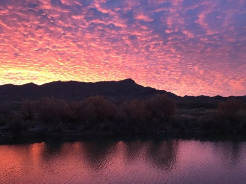 Vibrant sunset over a mountain, with colorful clouds reflecting in a calm river below.