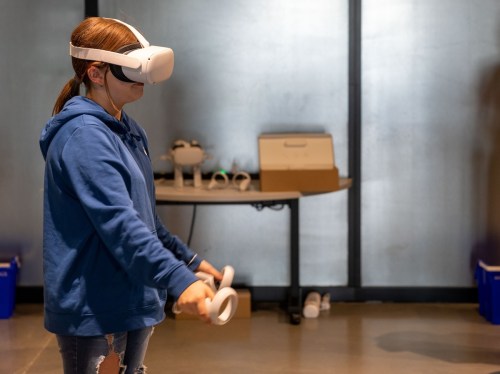 A person wearing a VR headset and holding controllers, engaged in a virtual reality experience indoors.