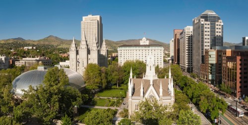 A panoramic view of a city skyline featuring modern buildings, a historic church, and green park spaces under a clear blue sky.