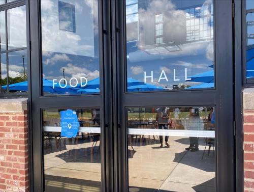 Entrance to a food hall with large glass doors and blue umbrellas visible outside.