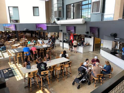 A spacious café with people dining, chatting, and a play area for children, featuring modern decor and large windows.