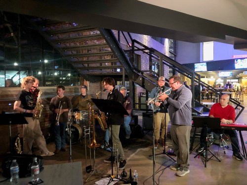 A jazz band performs indoors, featuring musicians with various instruments, including saxophones and a trumpet.