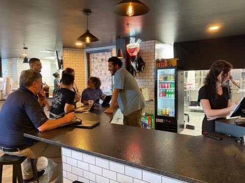 A busy café scene with customers at the counter and staff taking orders, featuring a modern interior design.