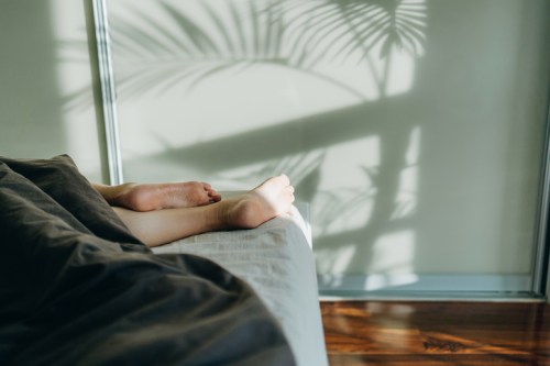 A pair of feet resting on a bed, with soft shadows of palm leaves on the wall.