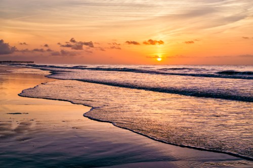 A serene beach at sunset, with gentle waves lapping at the shore and a colorful sky reflecting on the water.