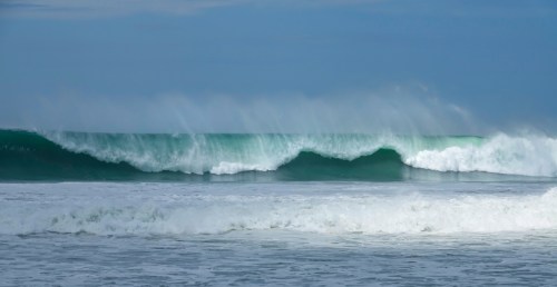 Waves crashing on a beach, with mist rising from the surf under a cloudy sky.