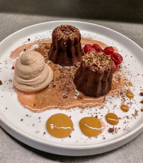 A plate with two chocolate lava cakes, a dollop of mousse, raspberries, and drizzles of caramel sauce.