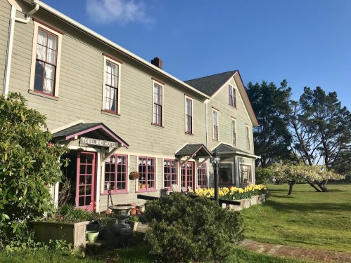 Historic Tokeland Hotel with pink trim, surrounded by greenery and blooming flowers under a clear blue sky.