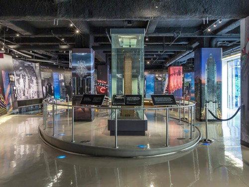 A modern exhibition space featuring displays about skyscrapers, with a central glass structure and informative panels.