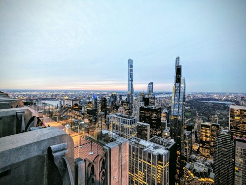 A panoramic view of a city skyline at dusk, featuring tall buildings and a cloudy sky.