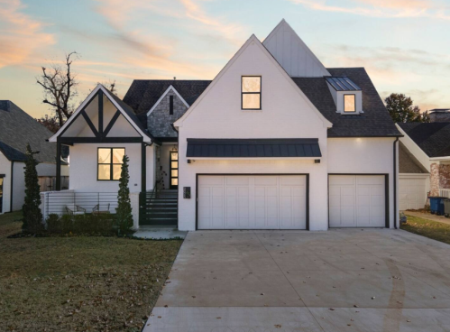 Modern two-story house with a white exterior, large garage, and a landscaped front yard at sunset.