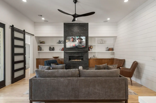 Modern living room with a gray sofa, wall-mounted TV, fireplace, and stylish decor. Bright and inviting atmosphere.