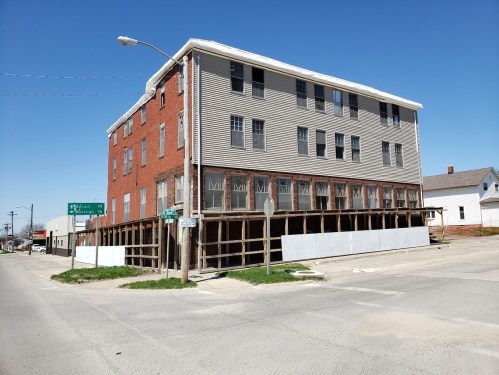 A three-story building with a mix of brick and siding, elevated on supports, located at a street intersection.