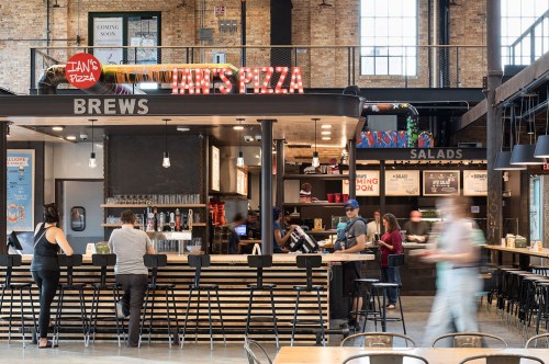 A modern pizza restaurant interior with a bar, menu boards, and customers ordering food in a vibrant space.