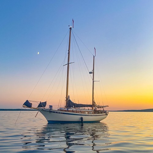 A sailboat anchored on calm waters during sunset, with a colorful sky reflecting on the surface.