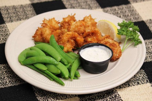 A plate of fried shrimp with a side of green snap peas, a lemon wedge, and a small cup of dipping sauce.