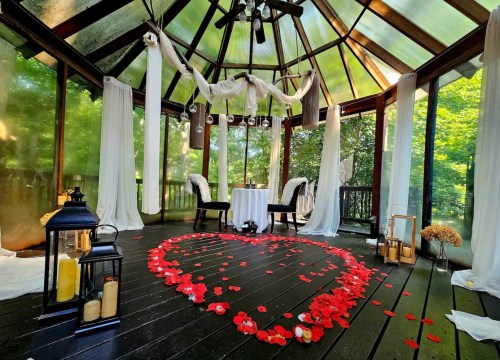 A romantic gazebo decorated with white drapes and red rose petals arranged in a heart shape on the floor.