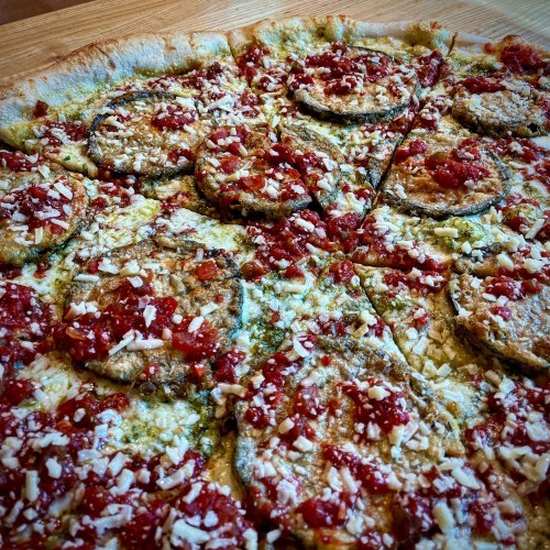 A close-up of a pizza topped with crispy eggplant, marinara sauce, and shredded cheese on a wooden surface.